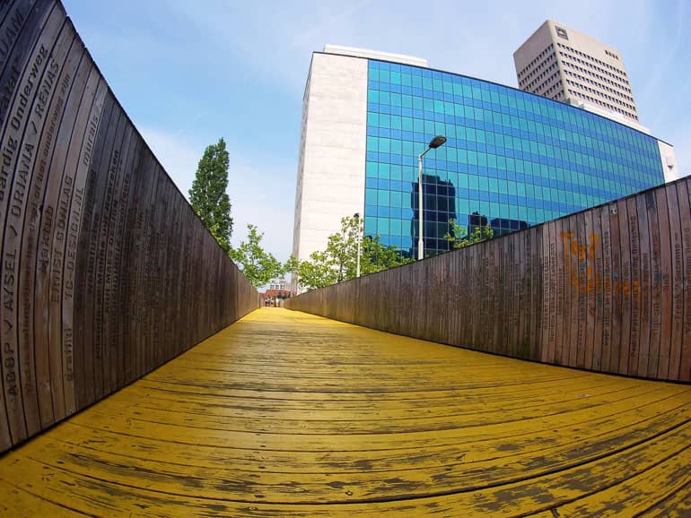 Die gelben Holzbrücke Luchtsingel in Rotterdam ist menschenleer, im Hintergrund ist ein Hochhaus zu sehen.
