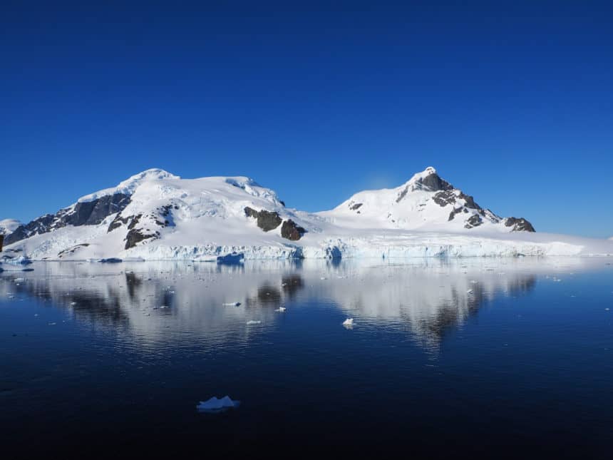 Die felsige und schneebedeckte Insel Cuverville Island spiegelt sich auf dem glasklarem Meer.