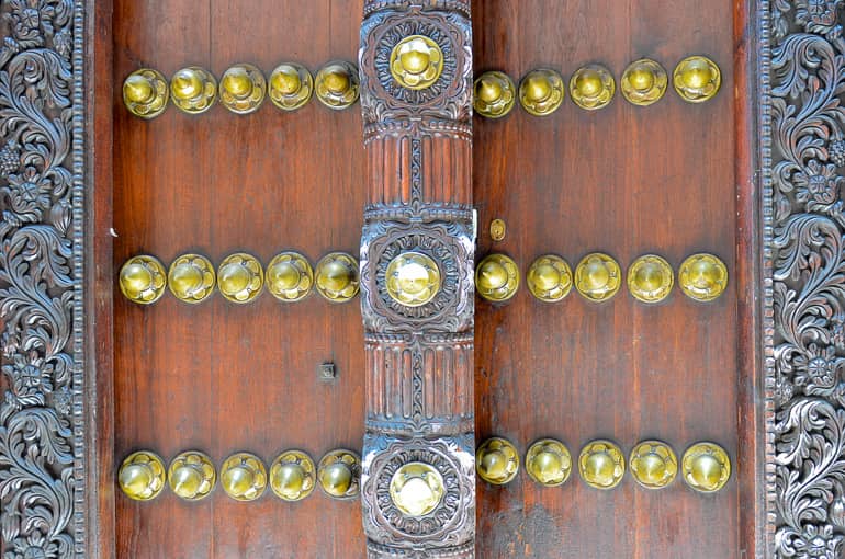 Eine verzierte Tür auf Sansibar, Tansania mit goldenen Knöpfen und ebenso verziertem Riegel.