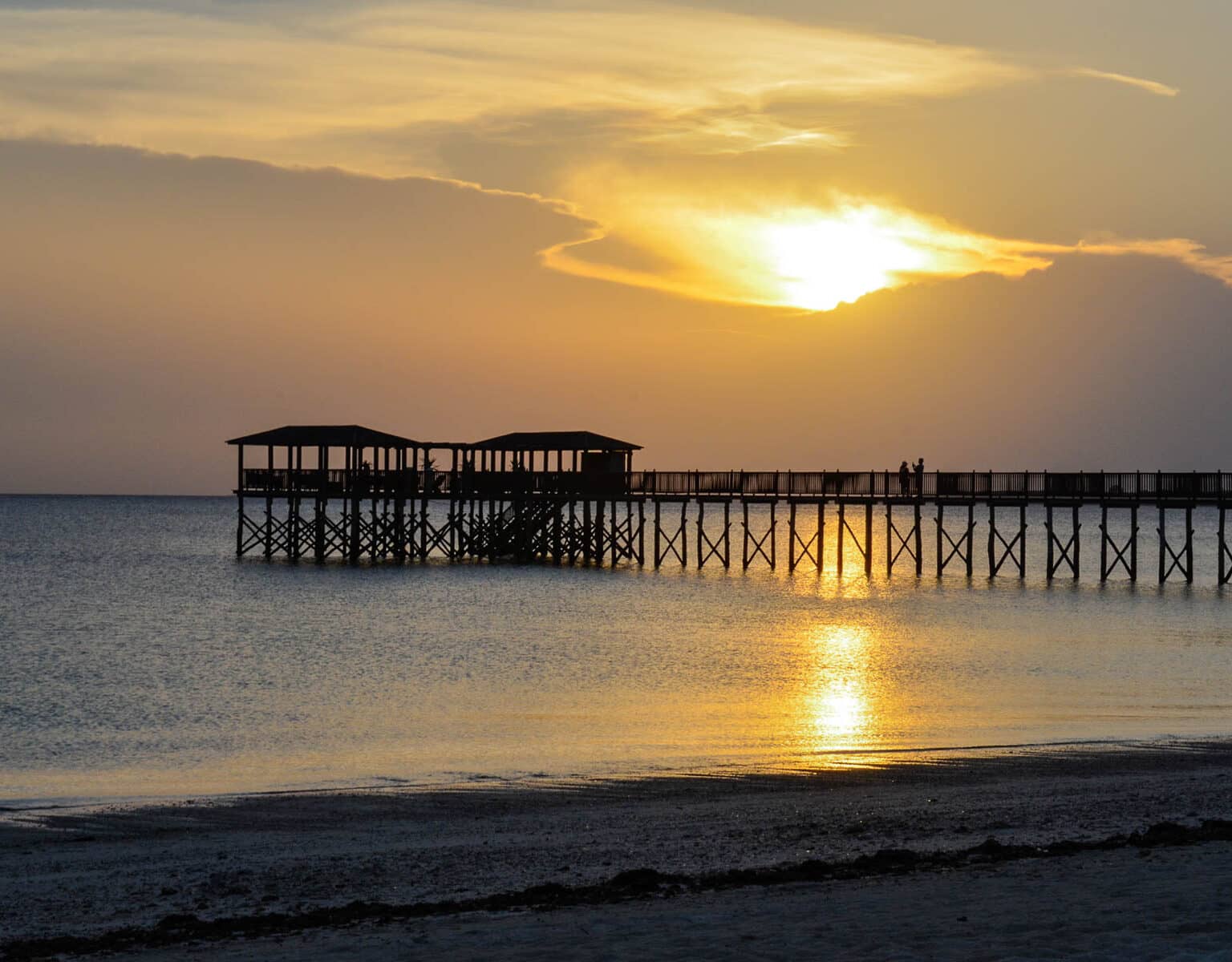 Sonnenuntergang auf Tansanias Sansibar, vom Strand führt einer hölzerner Steg mit Pavillion ins Meer.