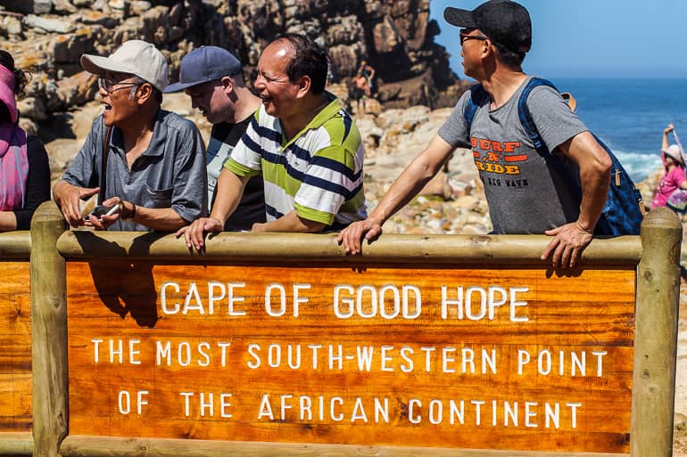 Asiatische Touristen posieren vor einem Schild, das den südwestlichsten Teil Afrikas markiert in Südafrikas Kapregion - Kap der guten Hoffnung.
