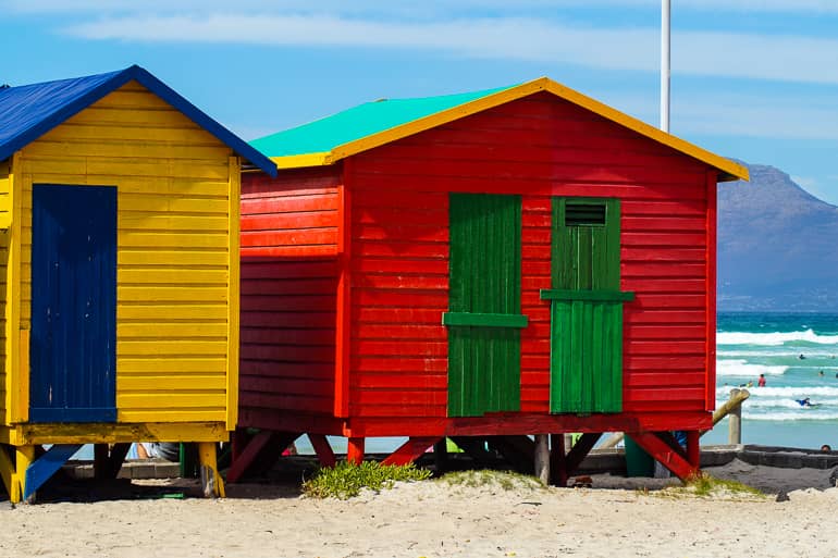 Am Sandstrand an der Kapregion Muizenberg Beach stehen zwei kleine bunte Strandhäuschen.