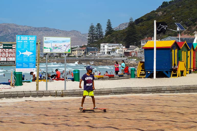 Am Strand von Muizenberg Beach fährt ein kleiner junge Skateboard.