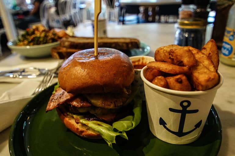 Ein großer Burger mit Kartoffelwedges steht auf einem Tisch im Restaurant The Boathouse in Manly, Australien.