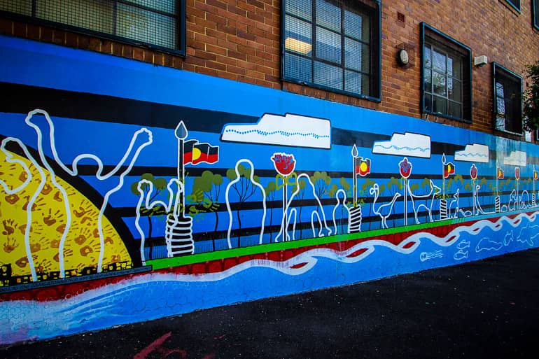 An einer Häuserwand in Redfern befindet sich ein Graffiti, auf dem weiße Linien die Konturen von Menschen darstellt.