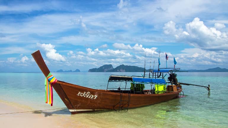 Am Strand von Koh Kradan hat ein Longtailboot, das mit bunten Bändern und Fahnen geschmückt wurde, angelegt.