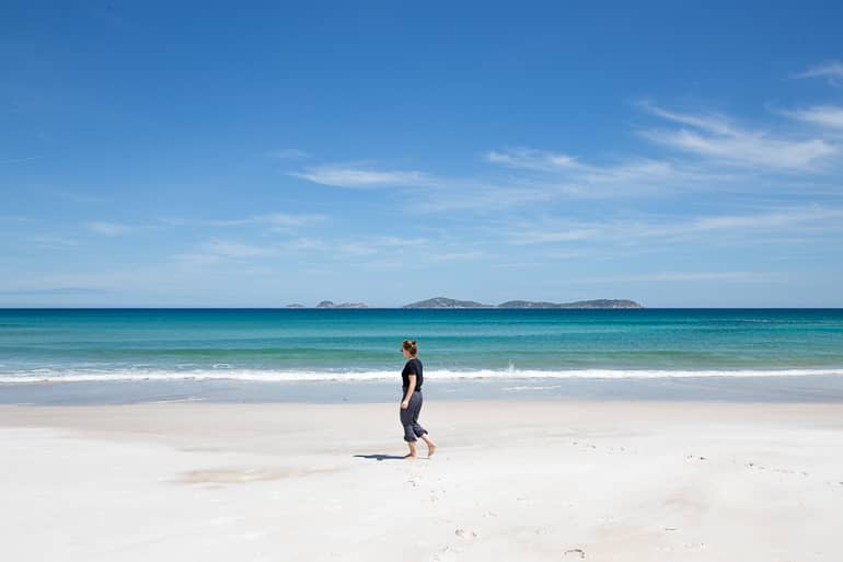 Die Bloggerin Anika wandert in Yarra Valley über den feinen, weißen Sandstrand von Squeaky Beach, das Meer schimmert in einem kraftvollem türkis.