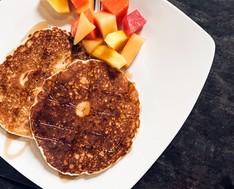Zwei Pancakes mit Ahornsirup und Melonenstückchen wurden auf einen weißen Teller angerichtet.