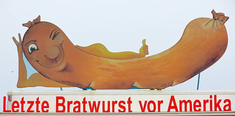 Ein Bratwurstschild an der Algarve zeigt eine liegende Bratwurst mit mit grinsendem Gesicht.