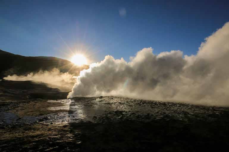Bei Sonnenuntergang steigt aus dem Geysirfeld El Tatio in Bolivien eine weiße Dampfwolke aus einer Bodenspalte.