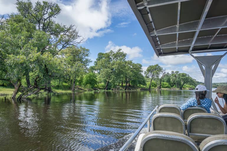 Ein Boot schippert auf dem Chobe River entlang, an Board sind zwei Touristen.