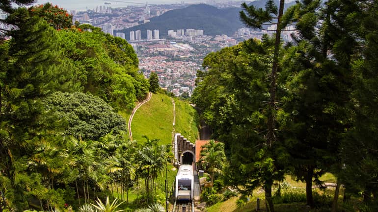 Malaysia: Eine Bahn fährt aus einem Tunnel kommend den Berg hinauf, im Hintergrund die Skyline.
