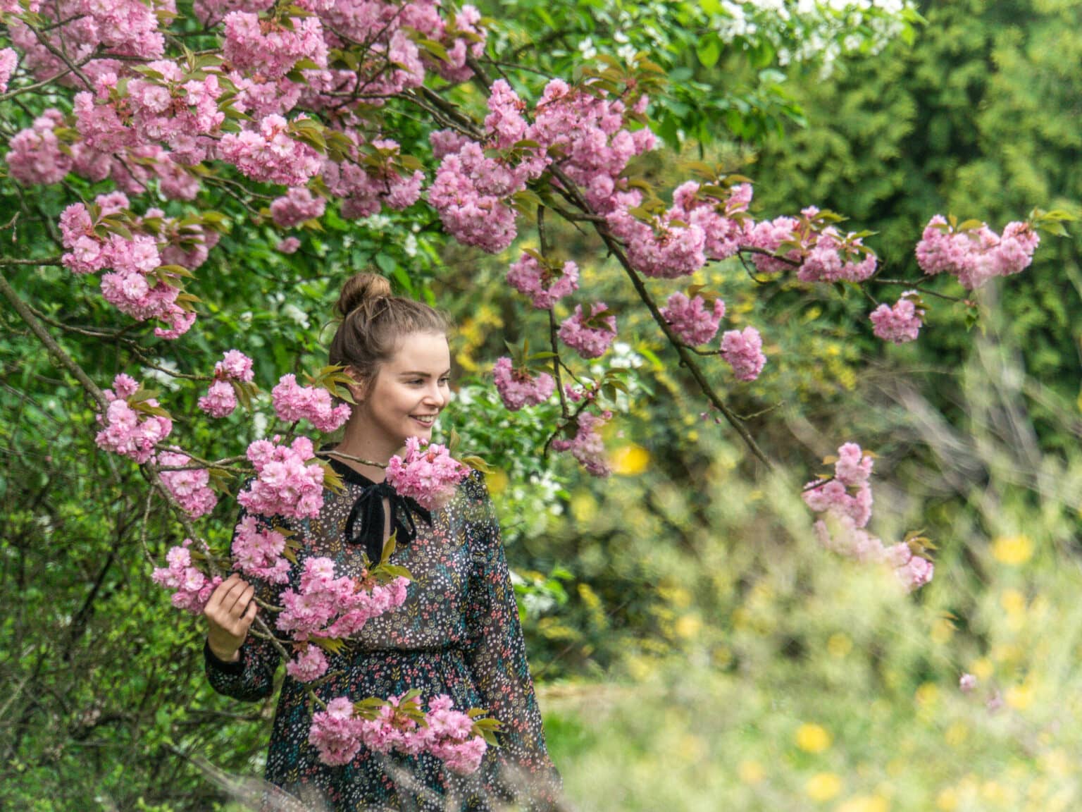 Eine Frau steht zwischen einem Baum an dem rosa Blumen hängen.