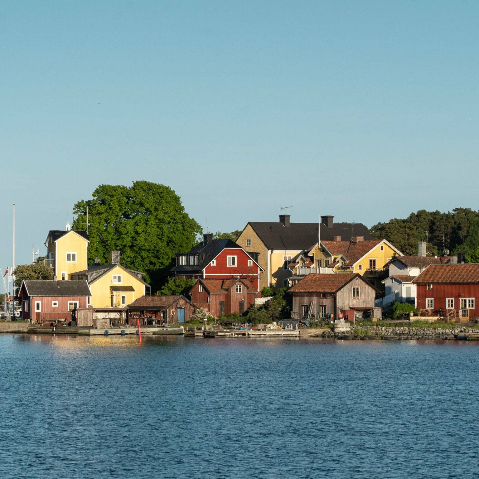 Ein kleines Dorf mit Holzhäusern in verschiedenen Farben und ein kleiner Hafen auf der Schäreninsel Sandhamn.