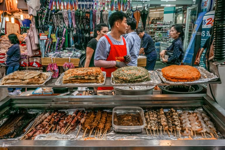Seoul Sehenswürdigkeiten: Ein Streetfood Stand mit gegrilltem Essen, ein Mann steht dahinter.