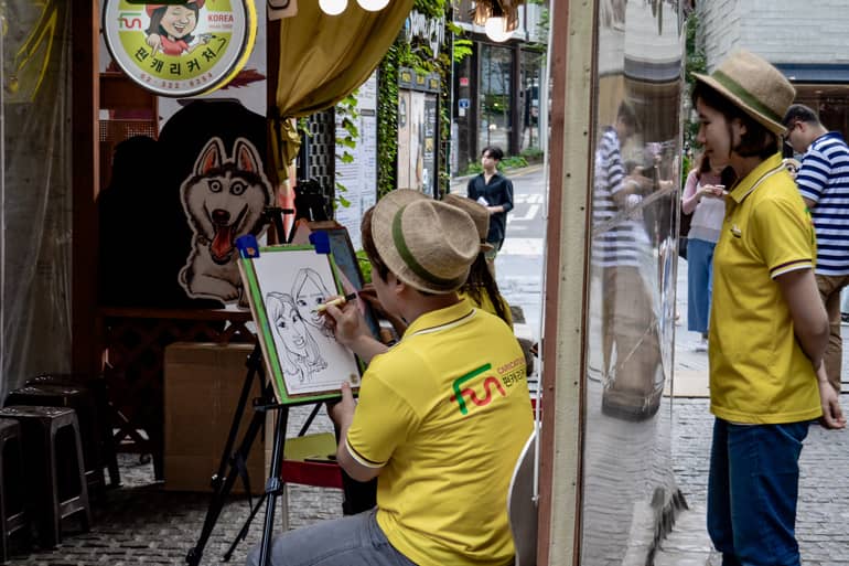 Straßenkunst in Seoul: Ein Mann zeichnet Gesichter auf einem Block, hinter ihm steht eine Frau.