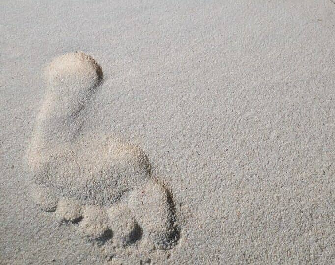 Ein einzelner Fußabdruck im Sand, dahinter das blaue Meer - beim allein Reisen lernt man viel über sich selbst.