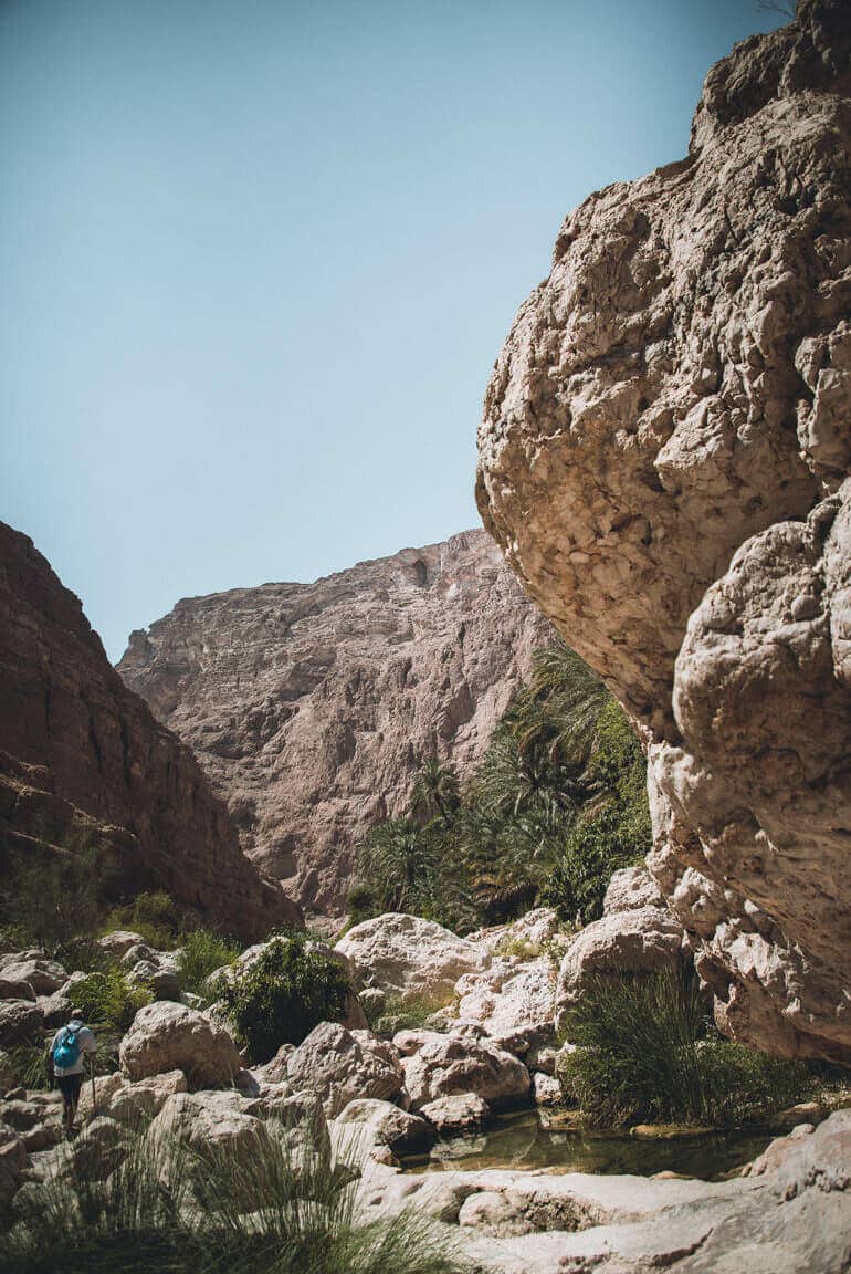 Ein Wanderer bahnt sich mit Gehstöcken den Weg durch Felsformationen der Wadi Shab im Oman.