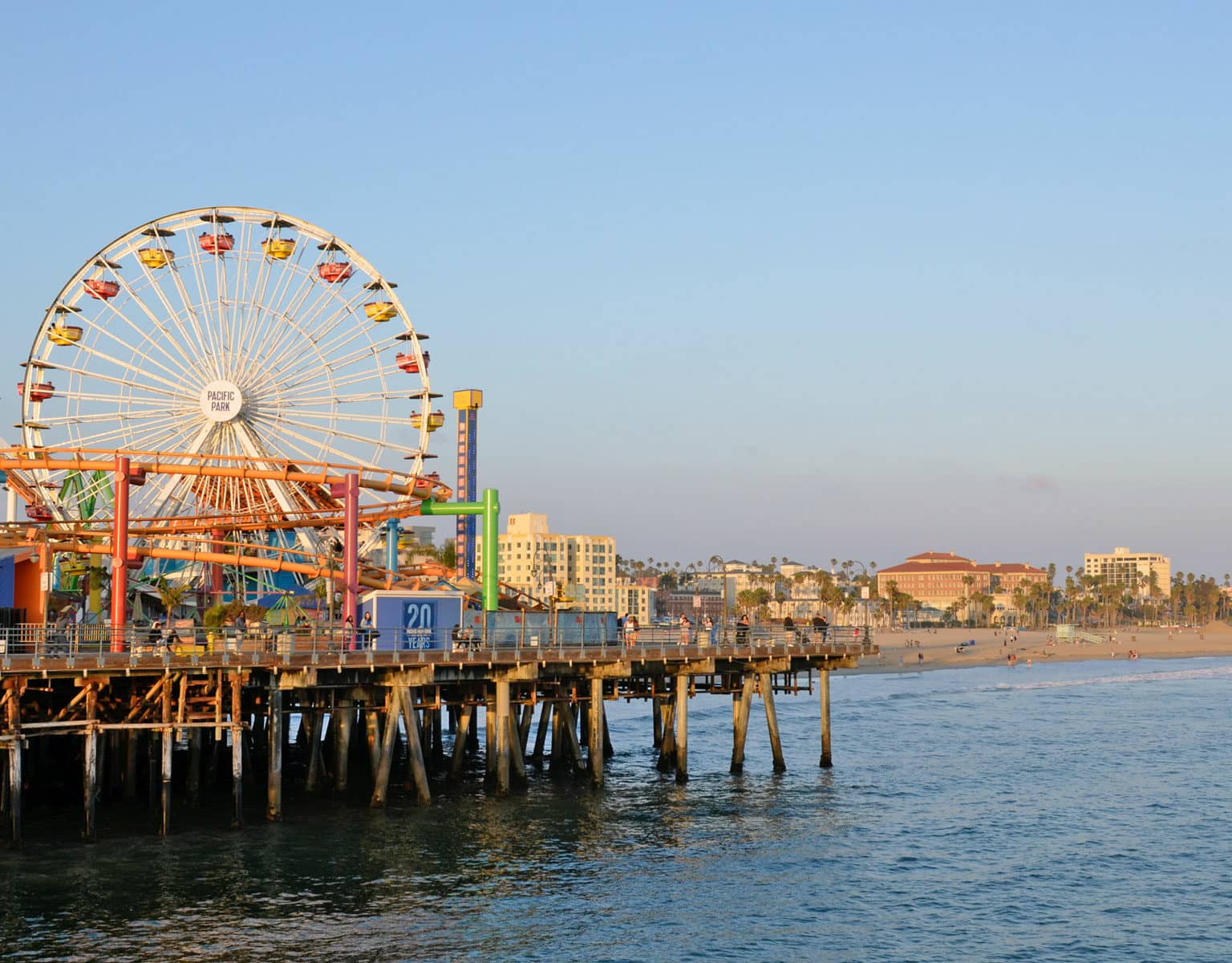 Fahrgeschäfte, darunter ein Riesenrad, auf dem berühmten Santa Monica Pier in der Nähe von Los Angeles, Kalifornien. Im Hintergrund leuchtet der Strand im Sonnenuntergang.