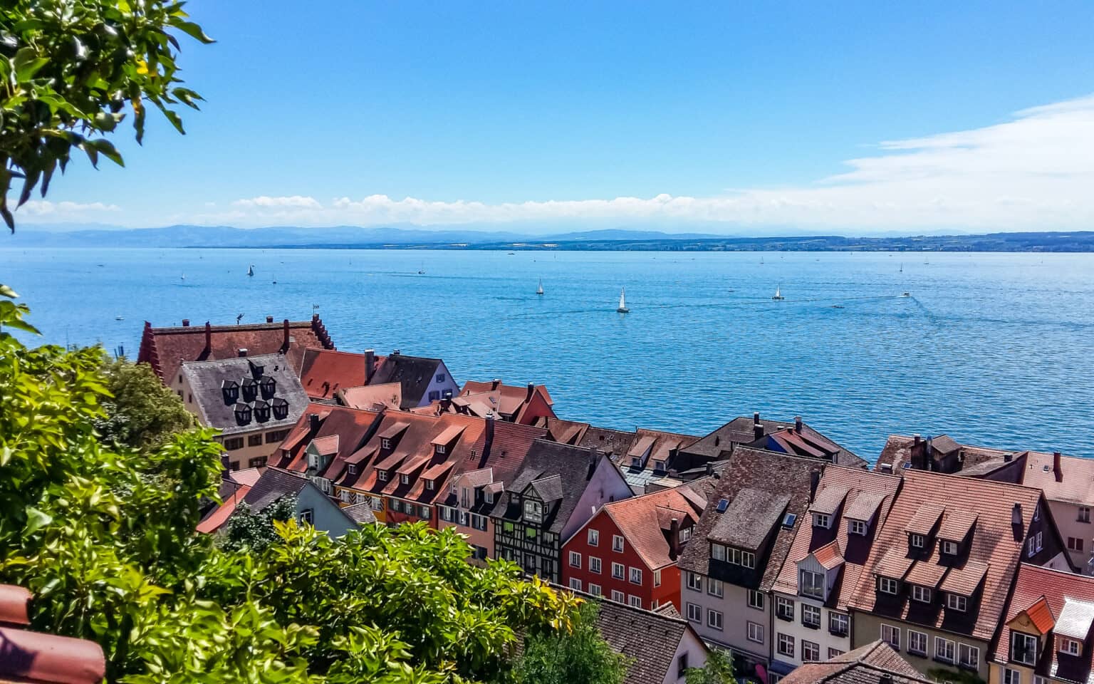 Der Blick über die Häuserdächer auf den Bodensee lässt ein paar vereinzelte Segelboote erkennen.