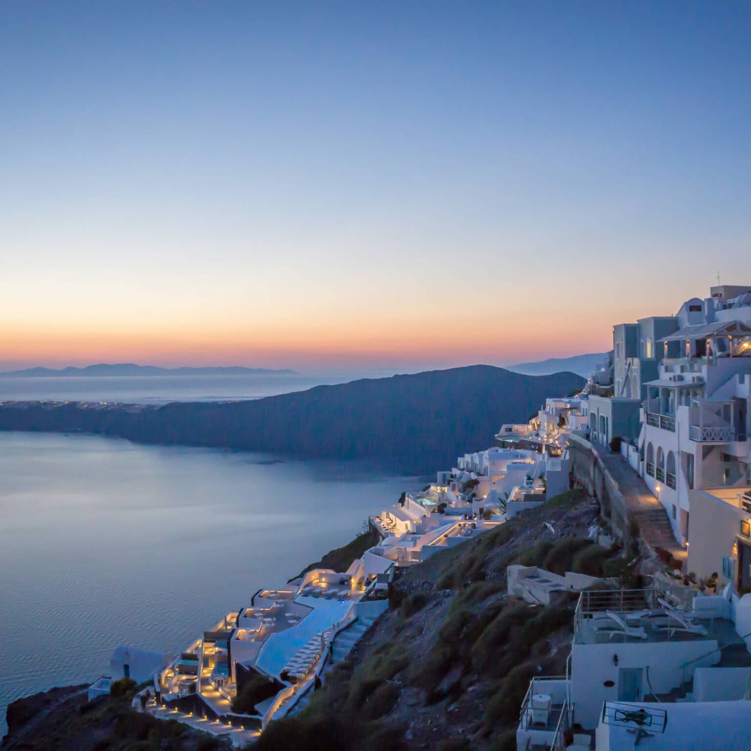 Über der Landzunge an der Kykladeninsel Santorini geht die Sonne unter und taucht die weißen Häuer in ein sanftes Licht.