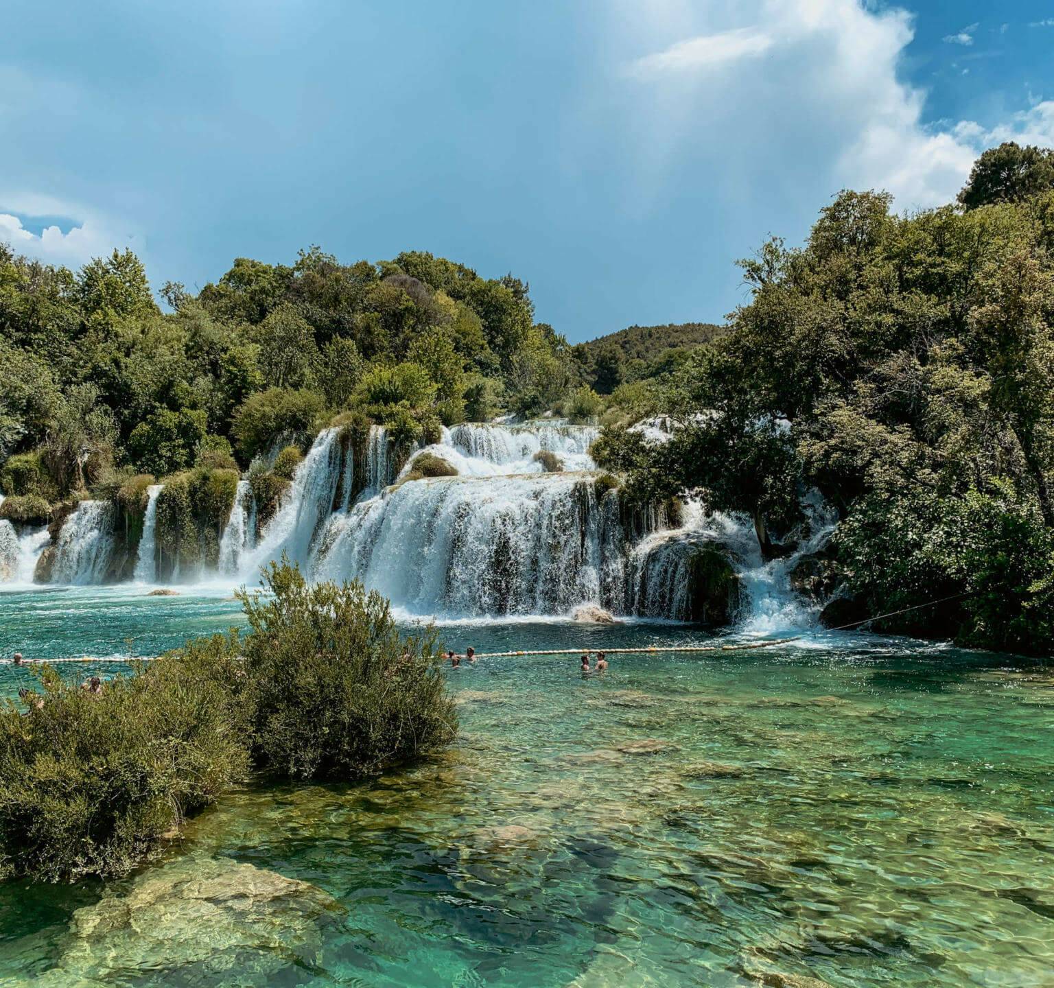 Hier muss man auf einem Roadtrip durch Kroatien einen Stopp einlegen: Der beeindruckende Wasserfall Skradinski Buk in Kroatien. In den Gumpen unterhalb des Wasserfalls schwimmen Besucher.