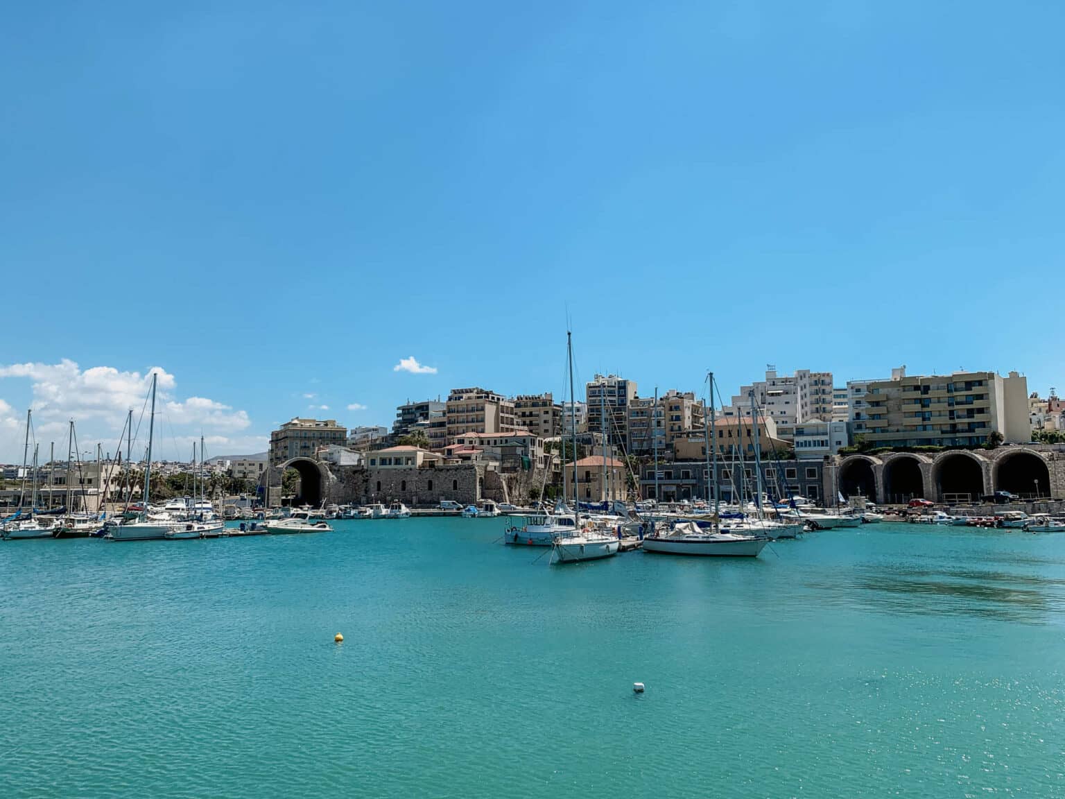 Zahlreiche Boote liegen im Hafen von Heraklion, der Hauptstadt von Kreta. Hinter dem Hafen stehen einige Hochhäuser.
