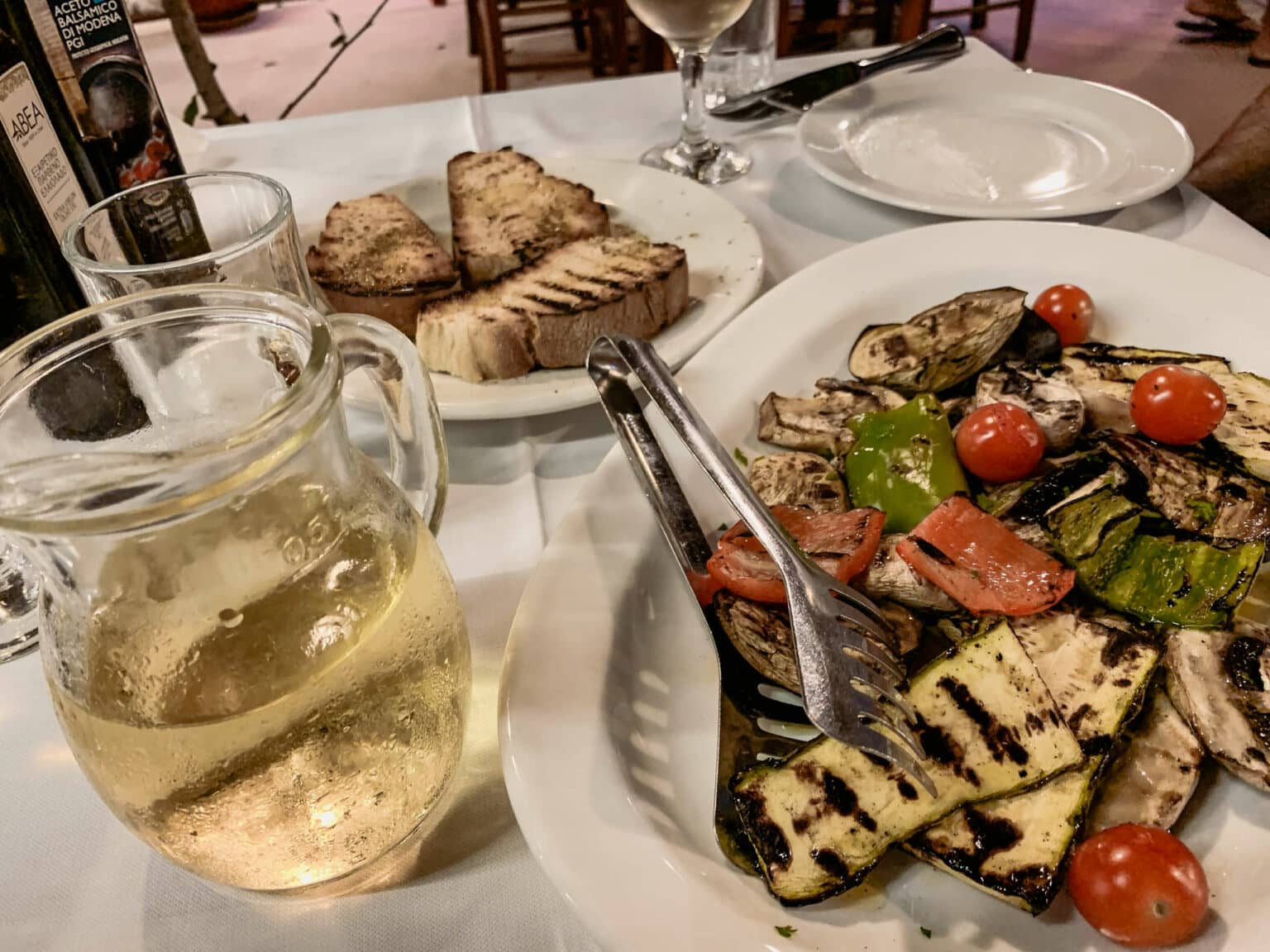 Auf einem Tisch angerichtetes Essen, geröstetes Gemüse, eine Karaffe mit Weißwein und Brot.