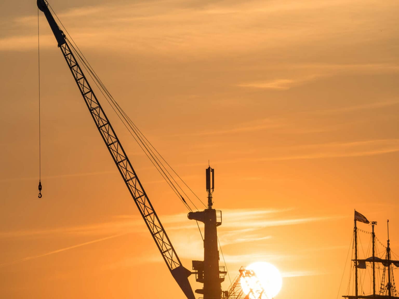 Ein alter Kran im Rostocker Hafen im Licht der untergehenden Sonne, der Himmel ist komplett orange gefärbt und wirft sein Licht auf den Kran.