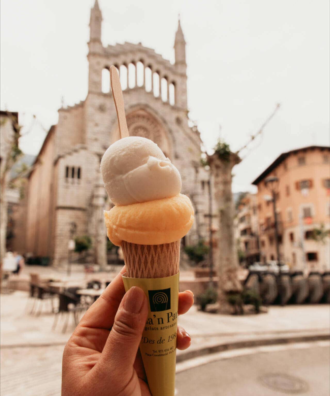 Auf dem Plaça Mercat Fet a Sóller auf Mallorca genießt Reisebloggerin Tatiana Eis in der Waffel, die Kirche Sant Bartomeu im Hintergrund.