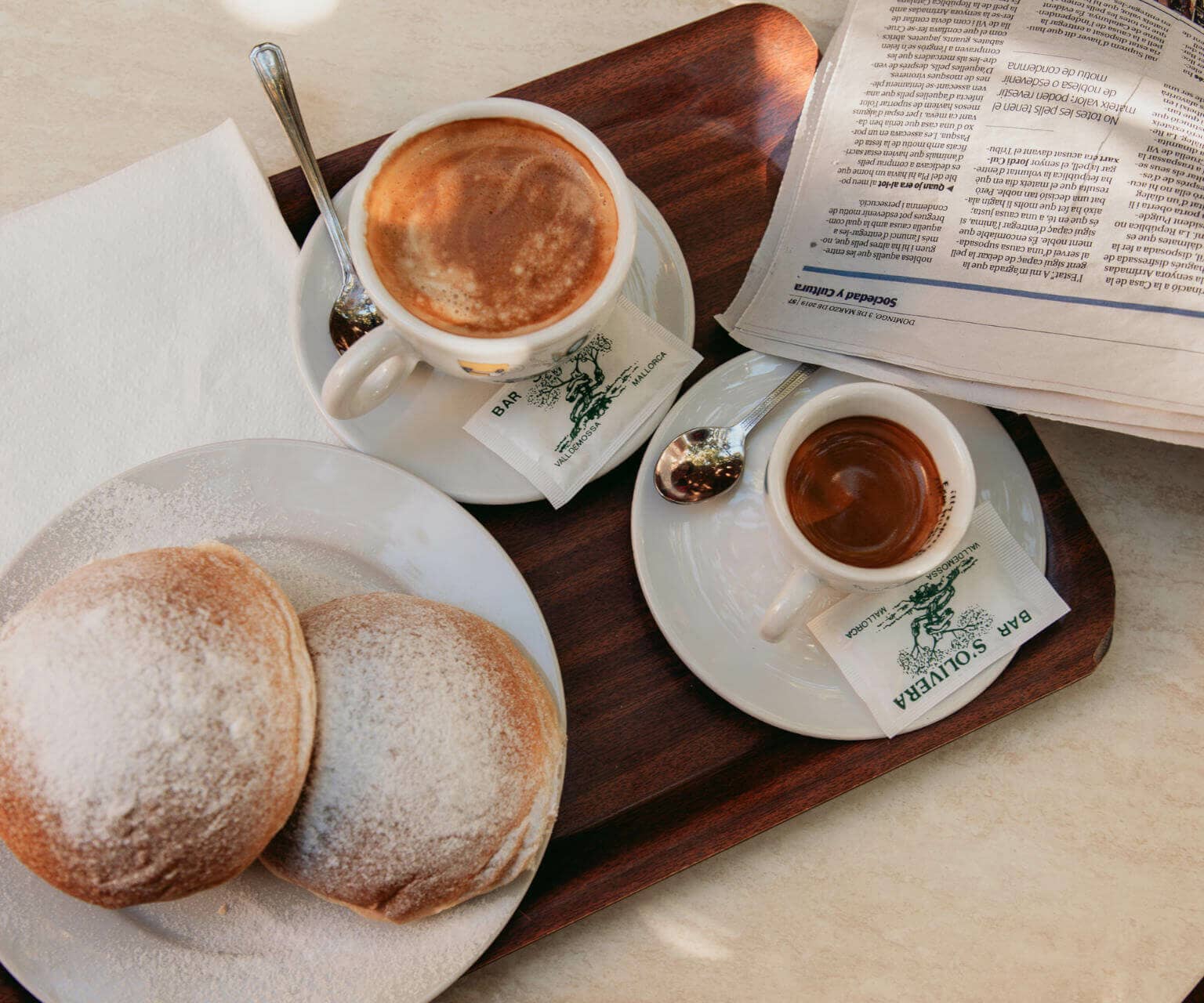 Hefebrötchen aus Kartoffelmehl, Cocas de Patata, mit Kaffee werden auf einem Holztablett in Mallorcas Ort Valldemossa serviert.