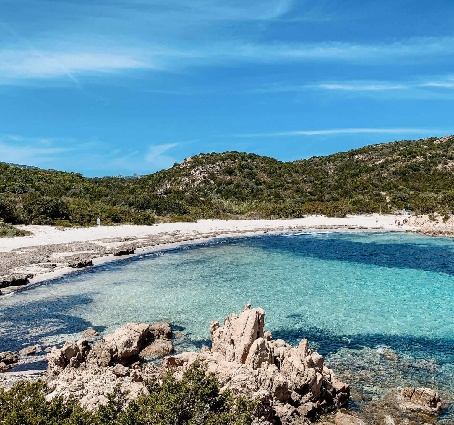 In der Bucht an der Spiaggia del Principe in Sardinien ist das strahlend blaue Wasser von Strand und Bergen umgeben.