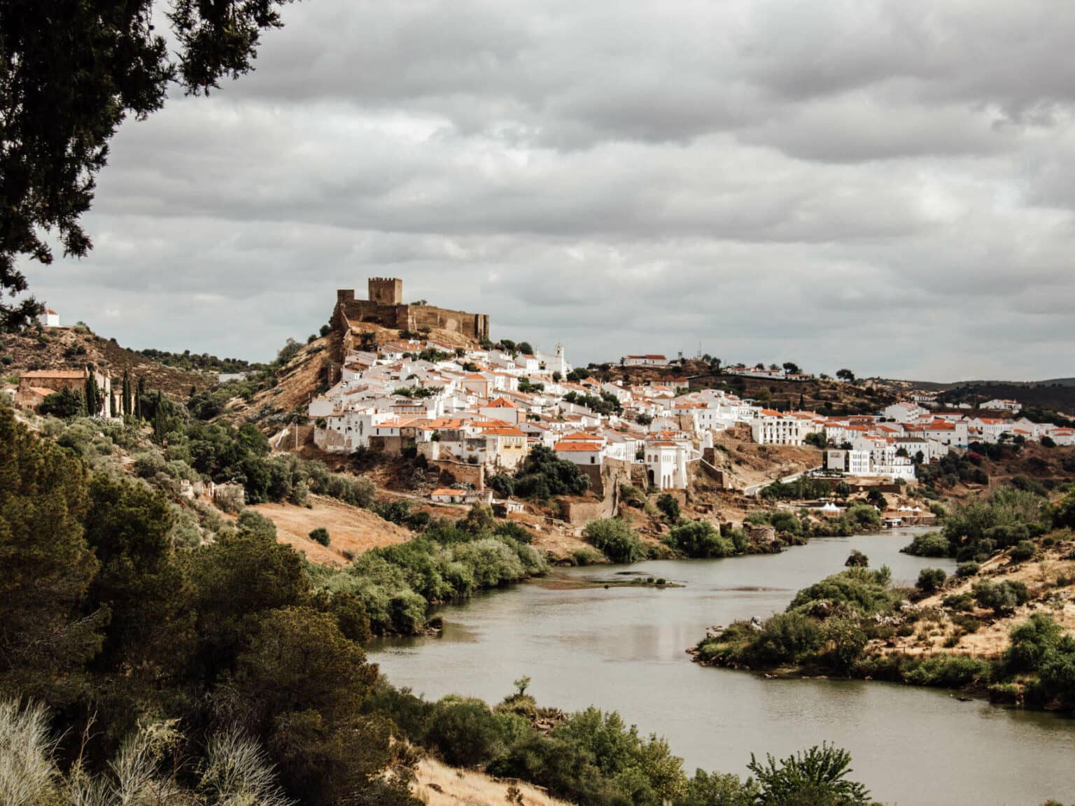 Eine Sehenswürdigkeit im Alentejo: Mértola. Ein sich schlängelnder Fluss vor dem Hügel einer Stadt im Alentejo.