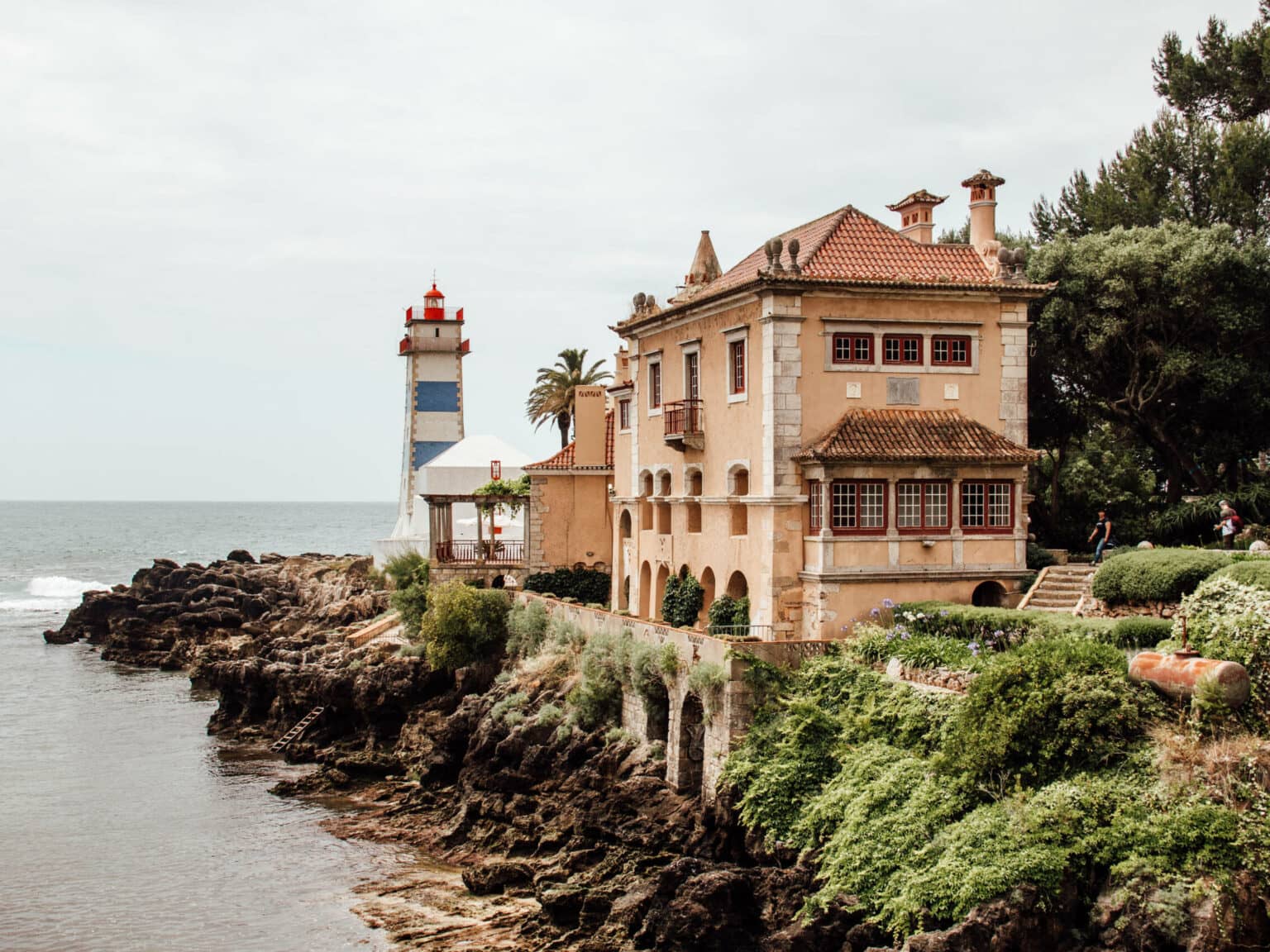 Ein sandfarbenes Haus entlang des Wassers mit abschließendem Leuchtturm. Ein Tipp für jeden Alentejo Roadtrip