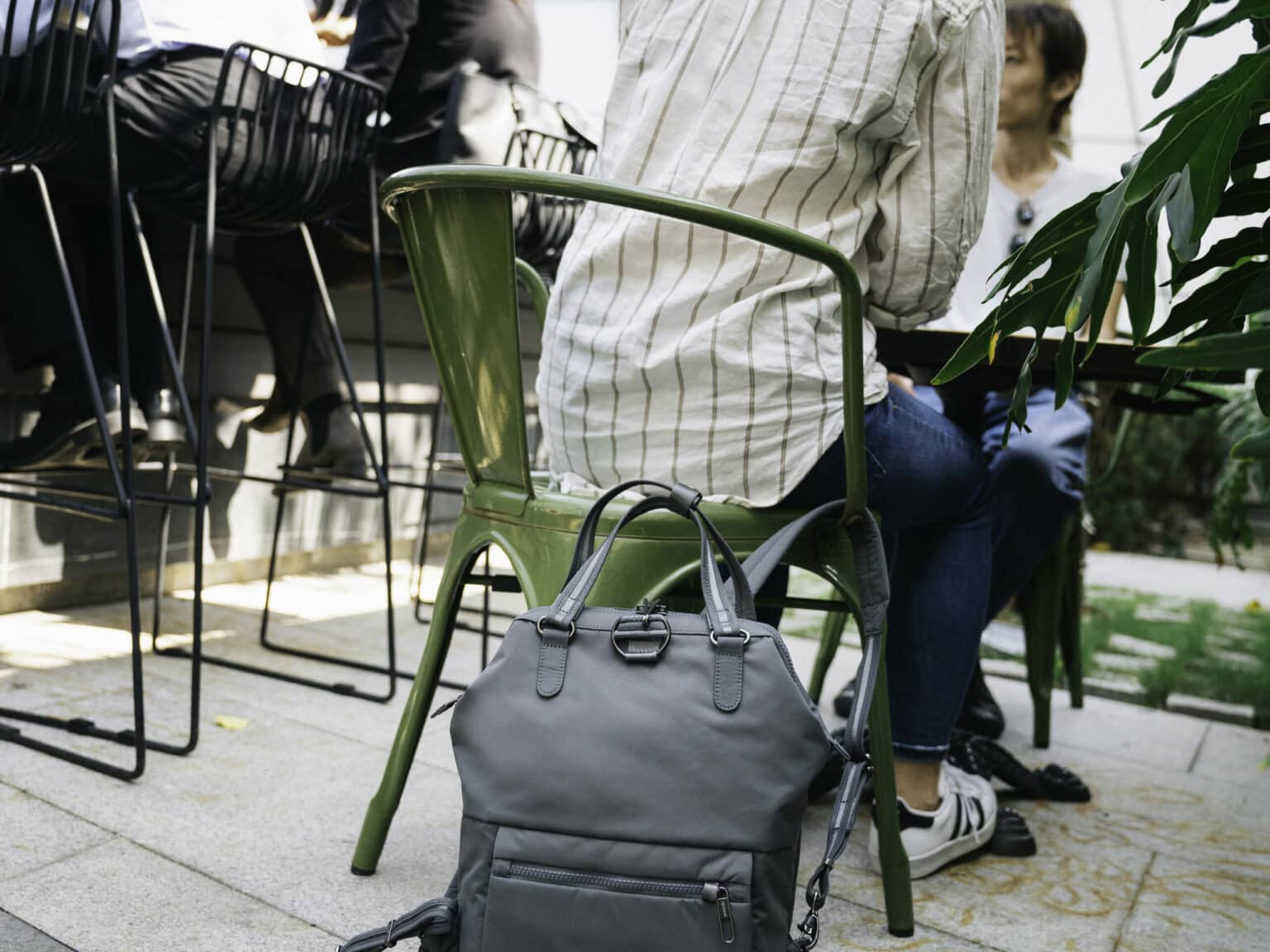 Eine Reisende kann dank des nützlichen Reise-Gadgets von Pacsafe ihren Rucksack am Stuhl befestigen.