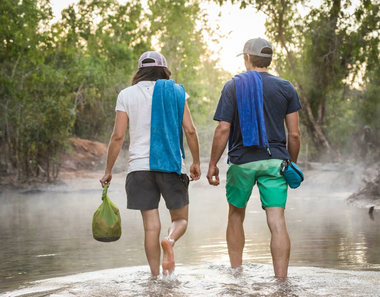 Zwei Reisende schlendern durchs Wasser, dabei einen Dry Bag, um die wertvollsten Gegenstände trocken zu halten - ein wahnsinnig nützliches Gadget auf Reisen.