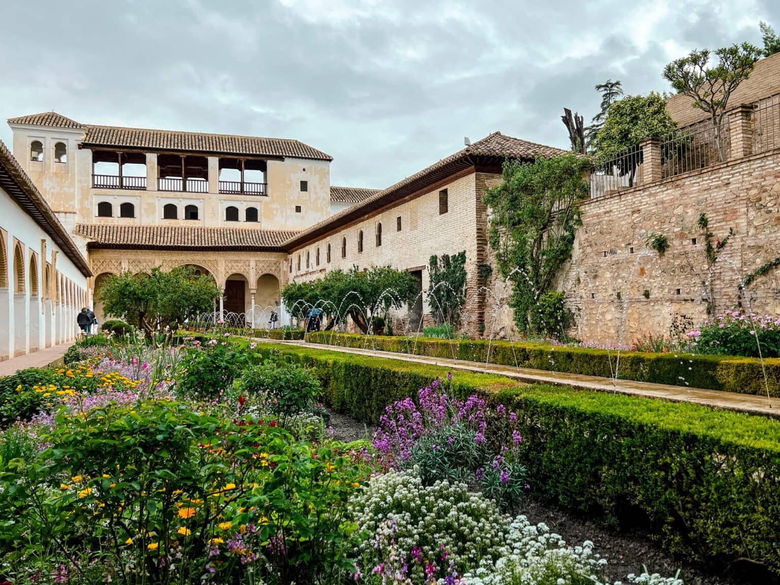 Ein farbliches Zusammenspiel aus grünen Hecken und gelb, rosa und weißen Blumen lassen den Palast im Generalife in der Alhambra erstrahlen.