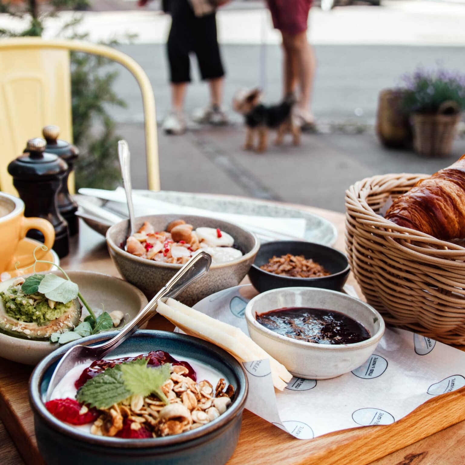 Das Frühstück mit Kaffee, Croissant, Avocado und Joghurt mit Müsli wird im Café Mad & Kaffe auf einem Holzbrett serviert.