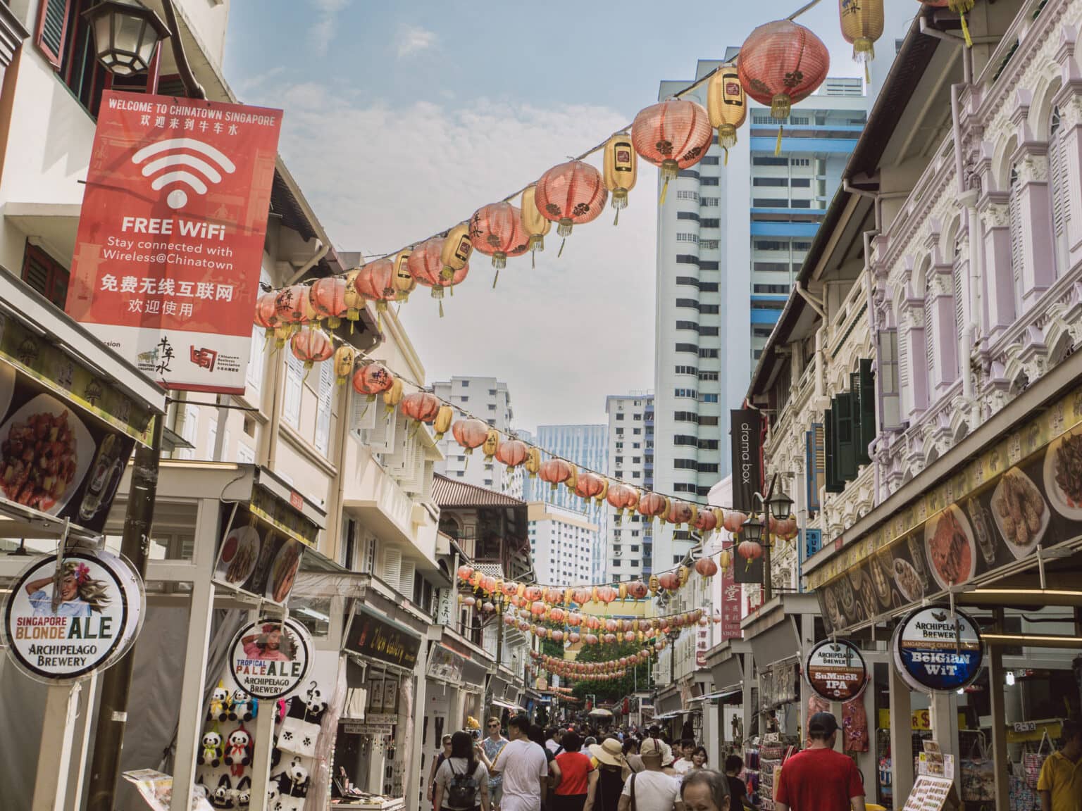 Gewusel in einer engen Straße und Lampions, die zwischen Gebäuden hängen in Chinatown in Singapur.