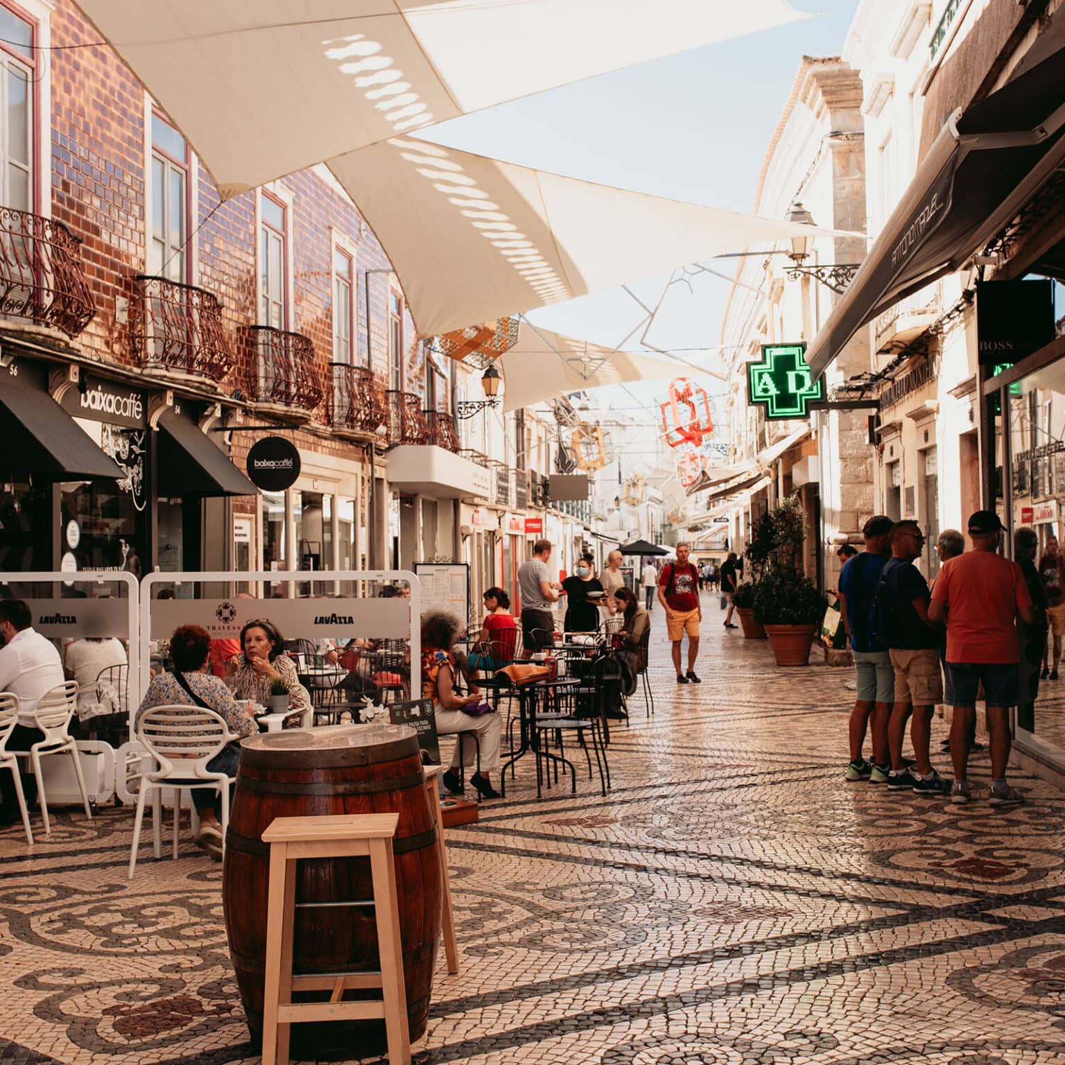 Menschen sitzen in Cafes in der belebten Einkaufsstraße Rua de Santo Antonio in Faro.