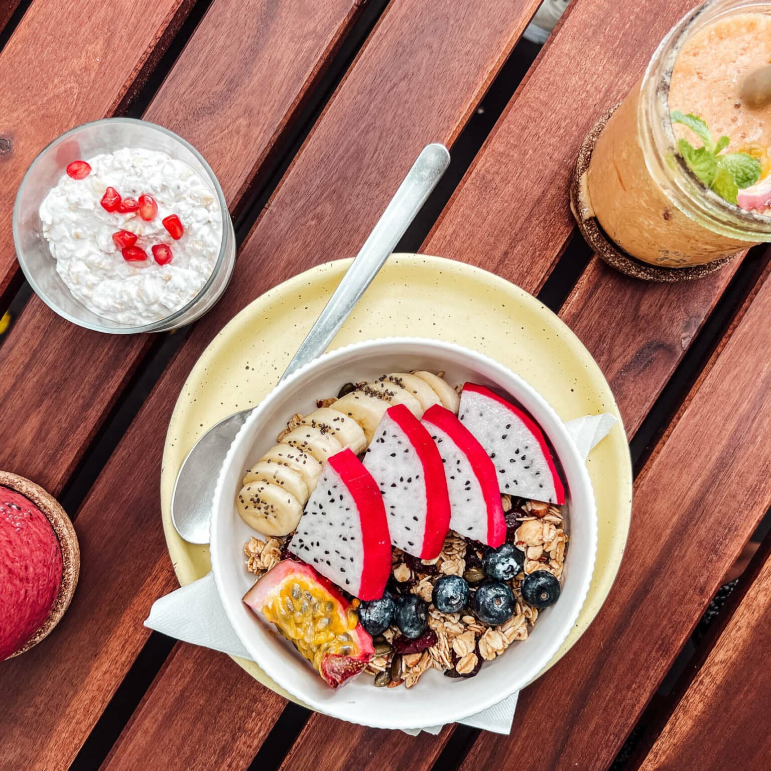 Eine Acai Bowl sowie zwei Smoothies stehen auf einem Holztisch.