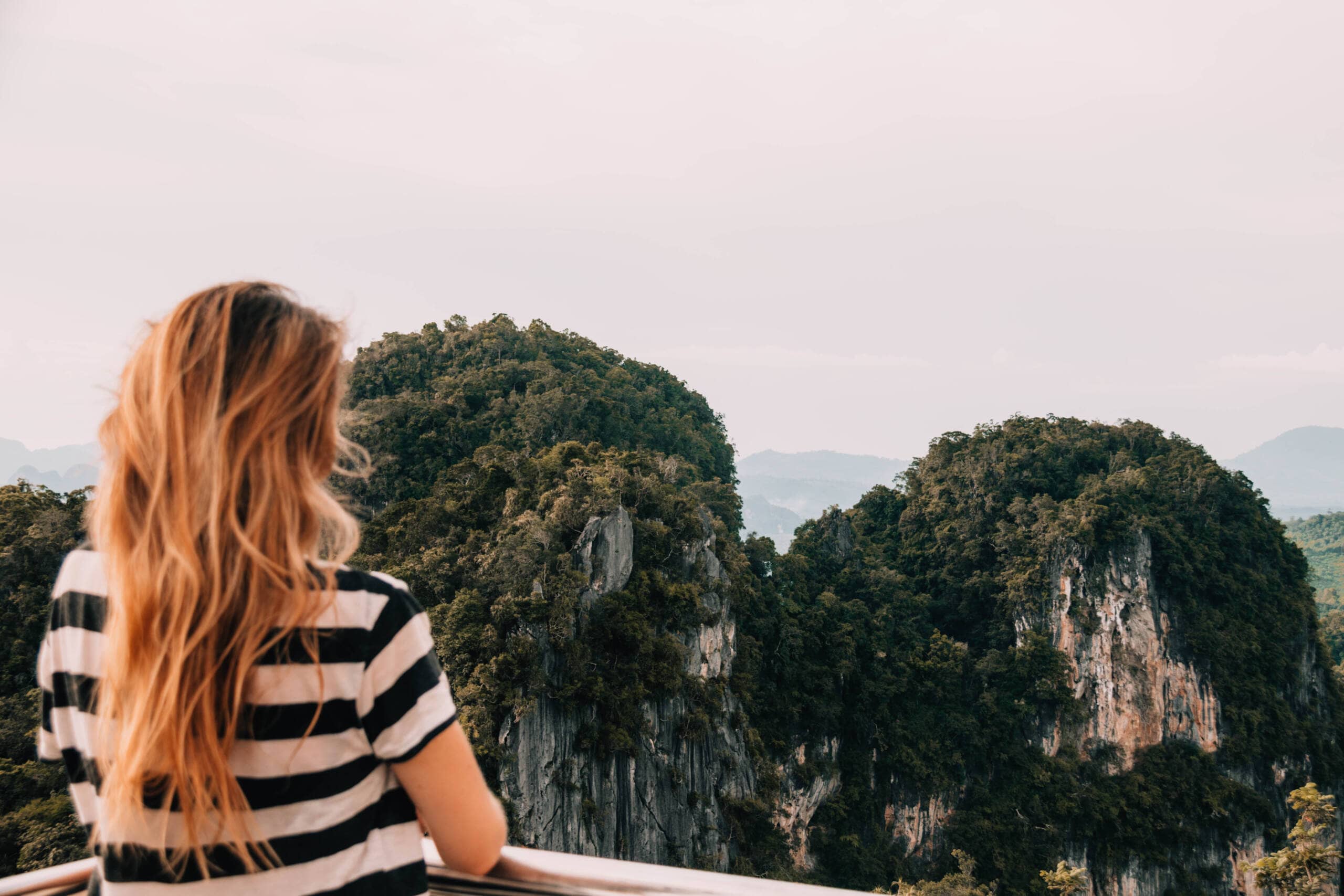 Eine blone Frau blickt auf die grünbewachsene Tiger Cave in Thailands Provinz Krabi.