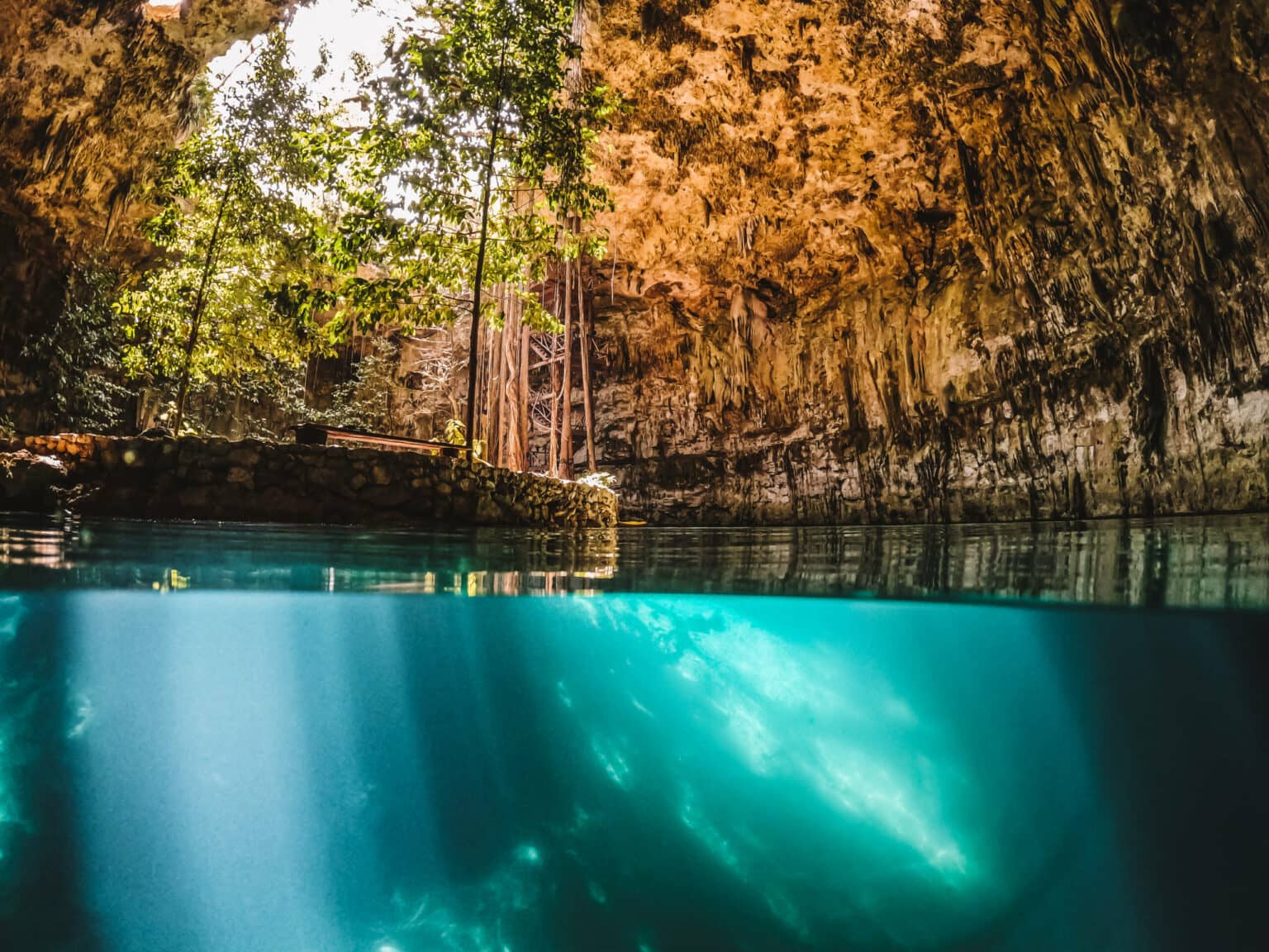 Türkisblaues Wasser im Vordergrund einer kleinen Insel mit Bäumen in der Cenote SAC-AUA.