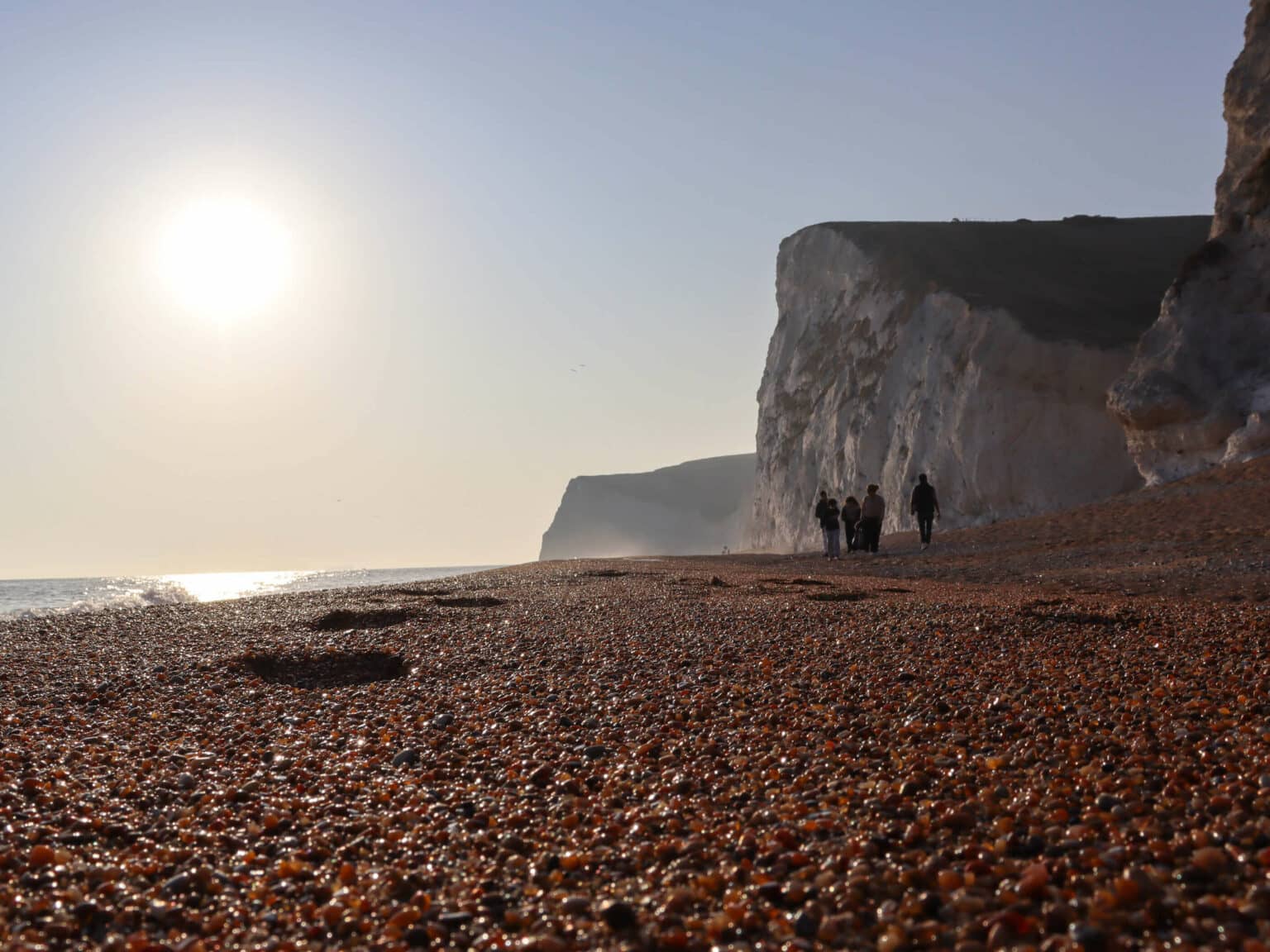 Ein paar Menschen laufen über den Kieselstrand Durdle Door-Beach in Südengland.