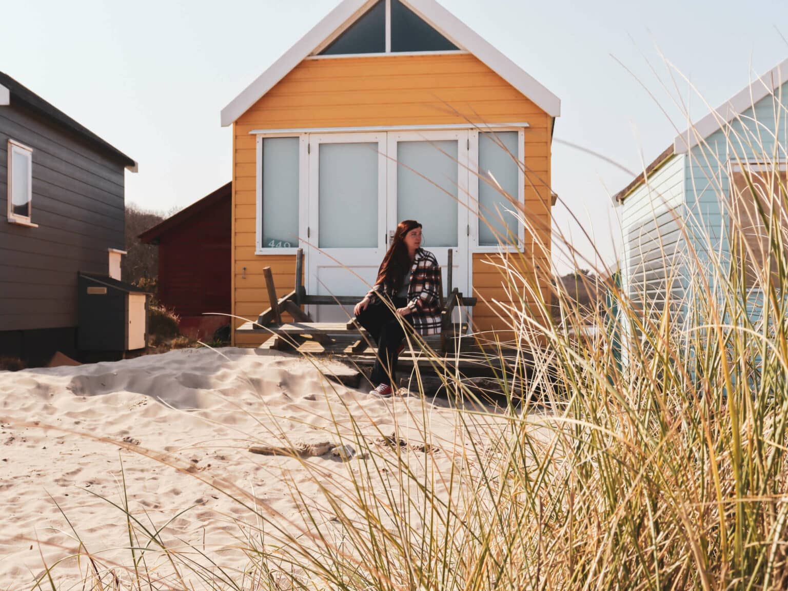 Eine Frau sitzt vor einer gelben Strandhütte im Mudeford Sands in Südengland.