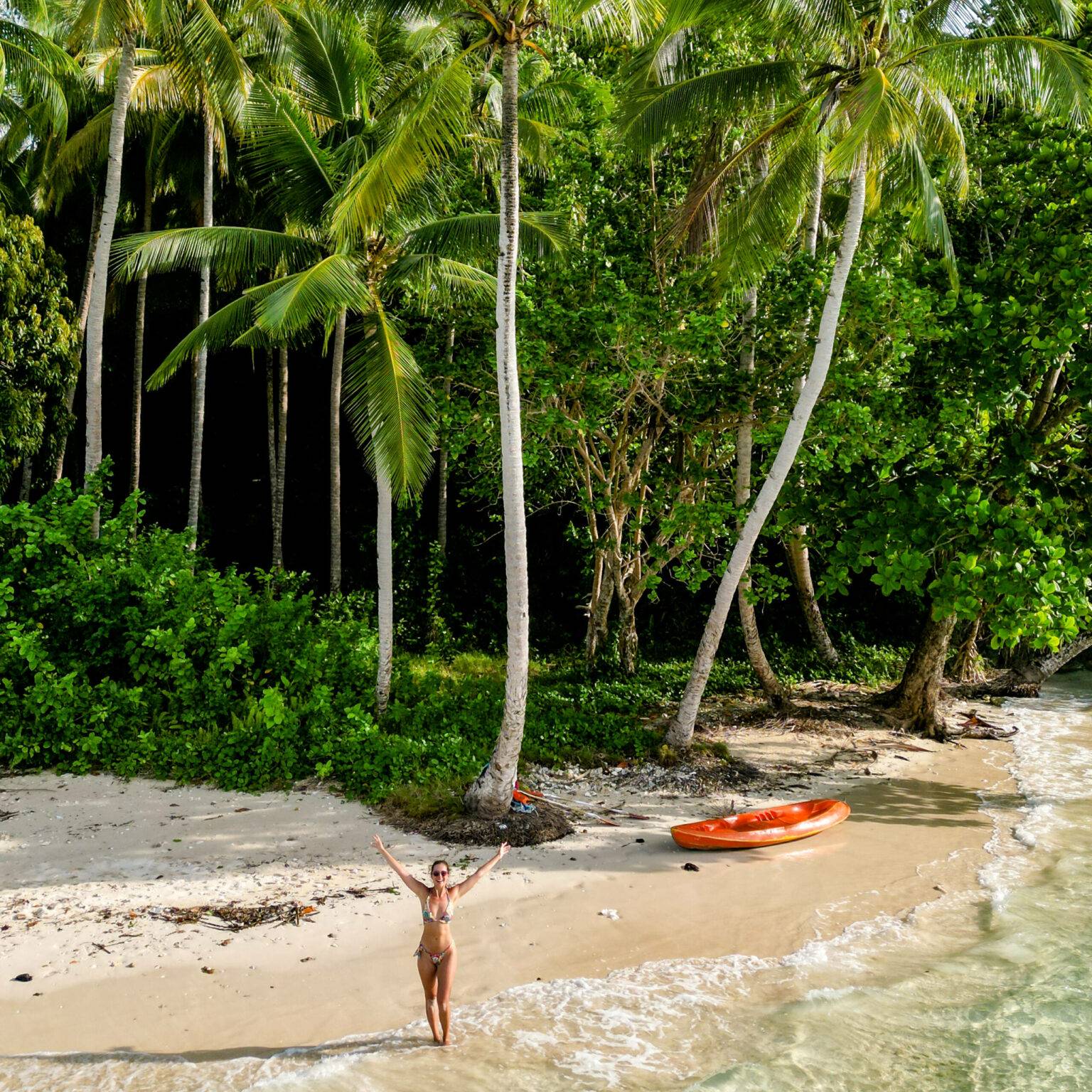 Bloggerin Nina steht an einem einsamen Strand auf Raja Ampat mit einem orangenen Kajak.