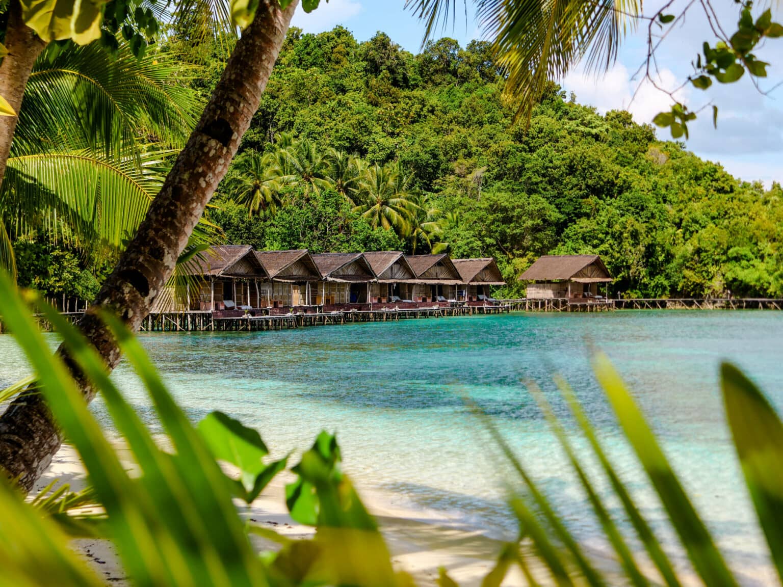 Holzhütten reihen sich an der türkisblauen Meeresküste von Raja Ampat.