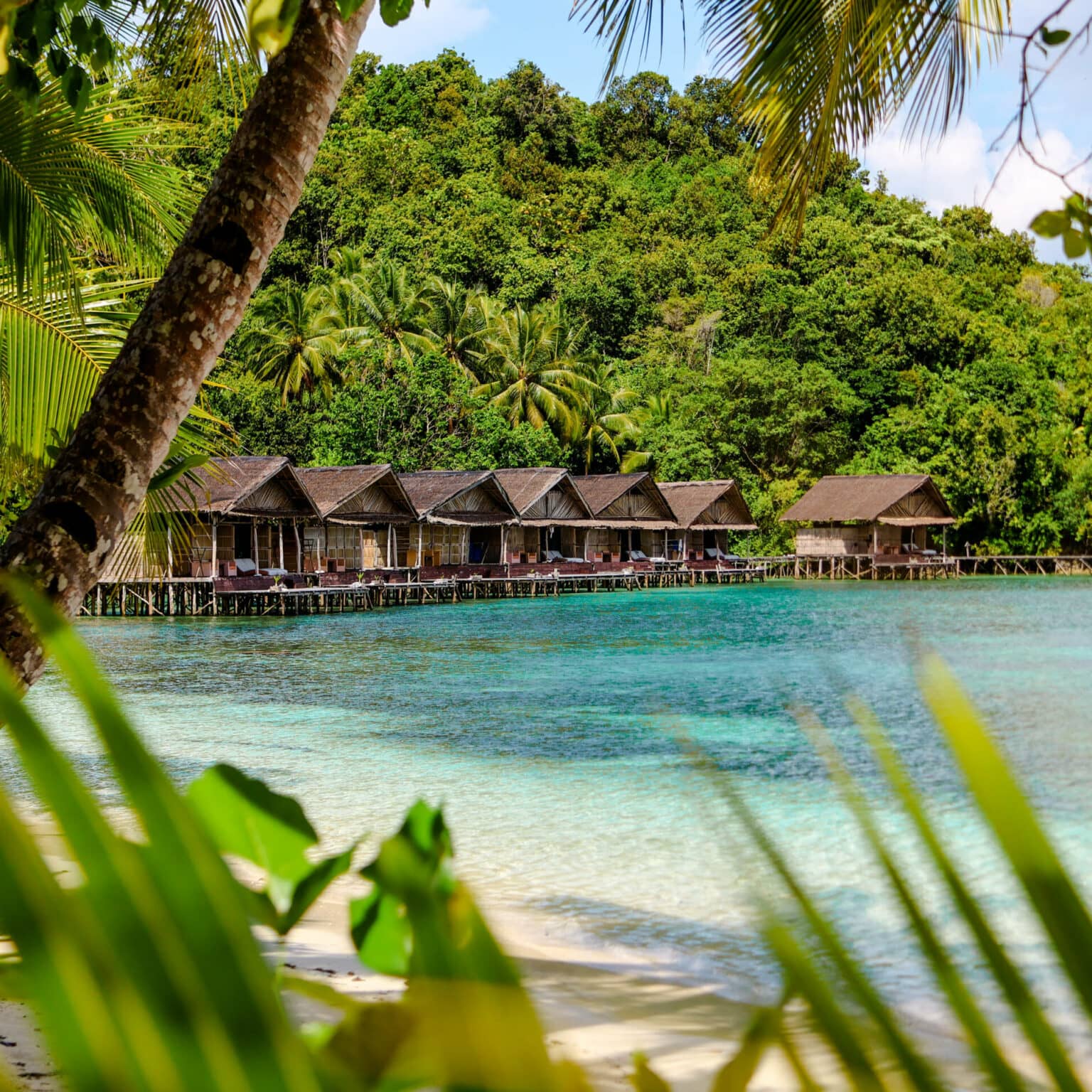 Holzhütten reihen sich an der türkisblauen Meeresküste von Raja Ampat.