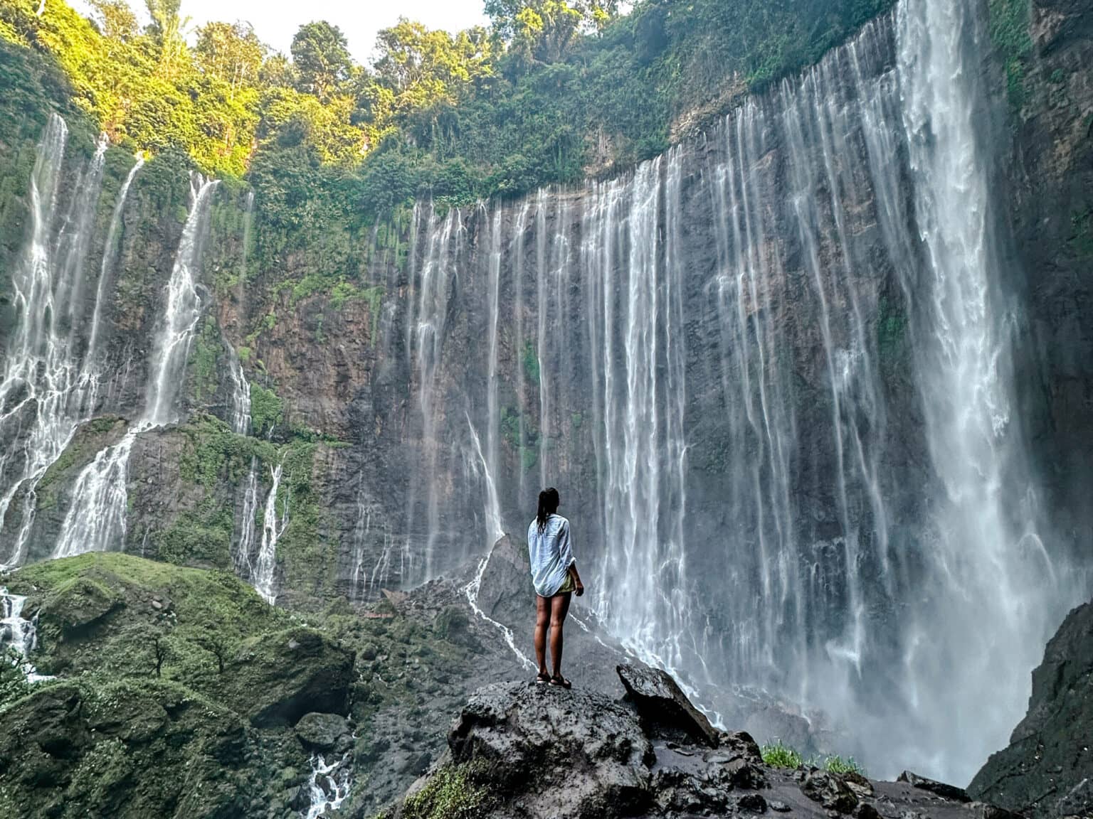 Bloggerin Nina steht auf einem Felsen und blickt auf den Tumpak Sewu Wasserfall in Java.