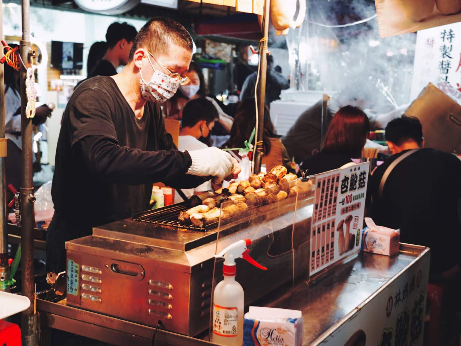 Ein Mann steht hinter einem kleinen Grill auf dem Austernpilze liegen auf dem Shilin Nachtmarkt in Taipeh.